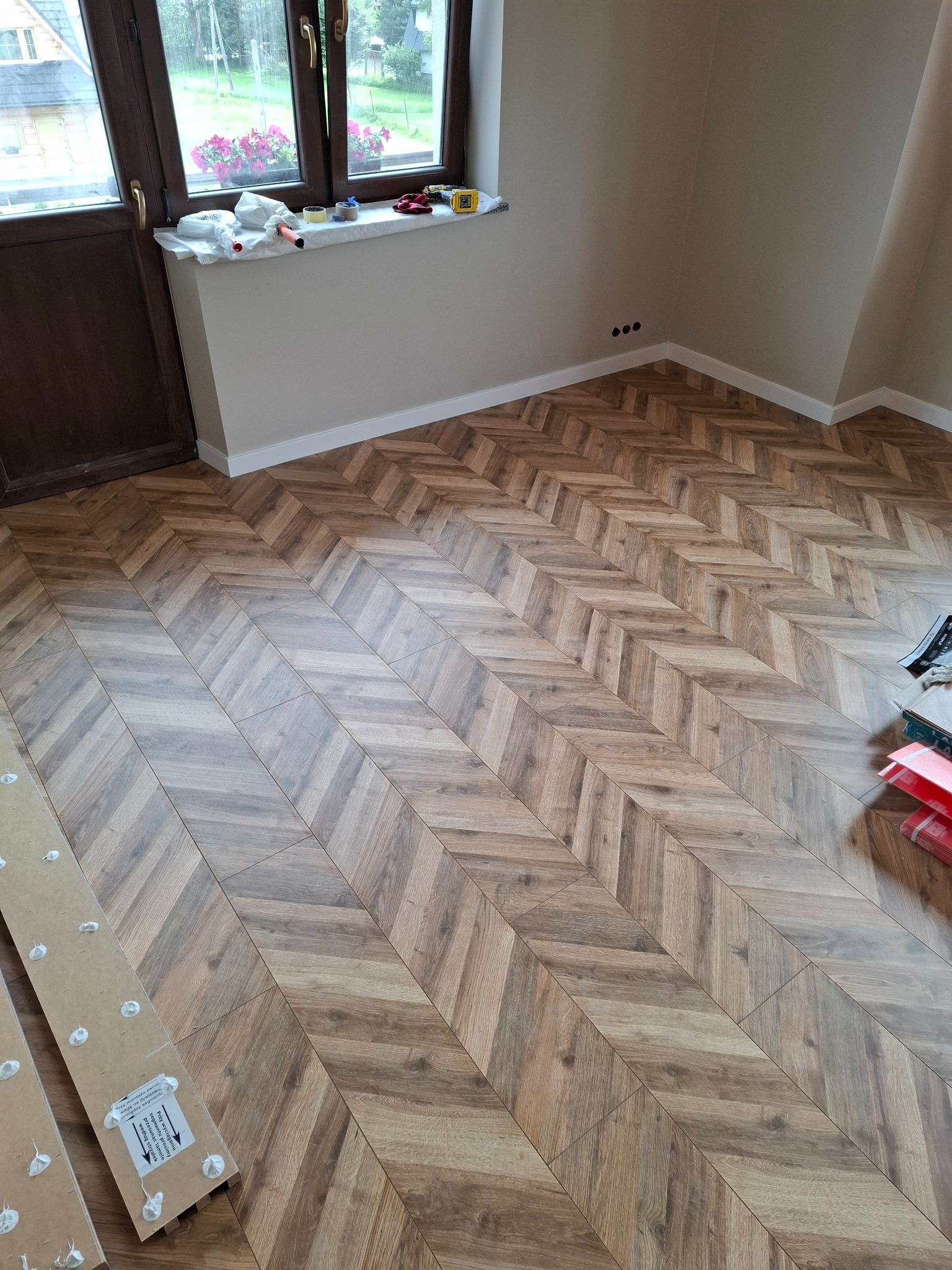 Ułożony parkiet w jodełkę w Ludźmierzu. Widoczne panele i akcesoria montażowe. Estetyczne wykończenie podłogi w nowym pomieszczeniu. Jasne, naturalne kolory.