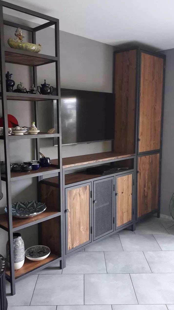 Regał z szafką RTV w stylu industrialnym: metalowa konstrukcja, drewniane fronty z elementami siatki, na półkach dekoracyjne naczynia i ceramika.