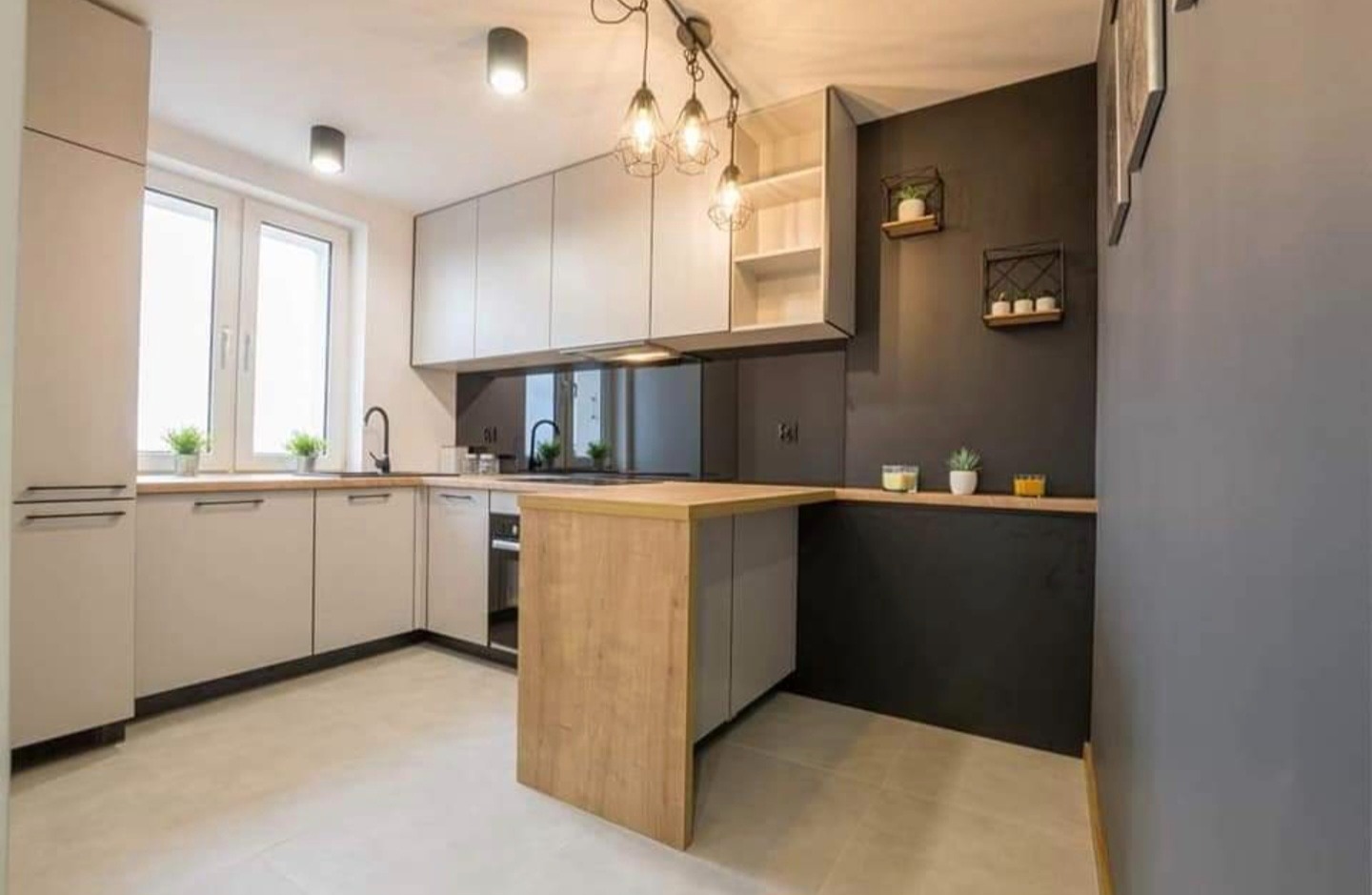 Nowoczesna kuchnia z szarymi szafkami, drewnianym blatem i wyspą, oświetleniem punktowym i dekoracyjnymi półkami na czarnej ścianie.