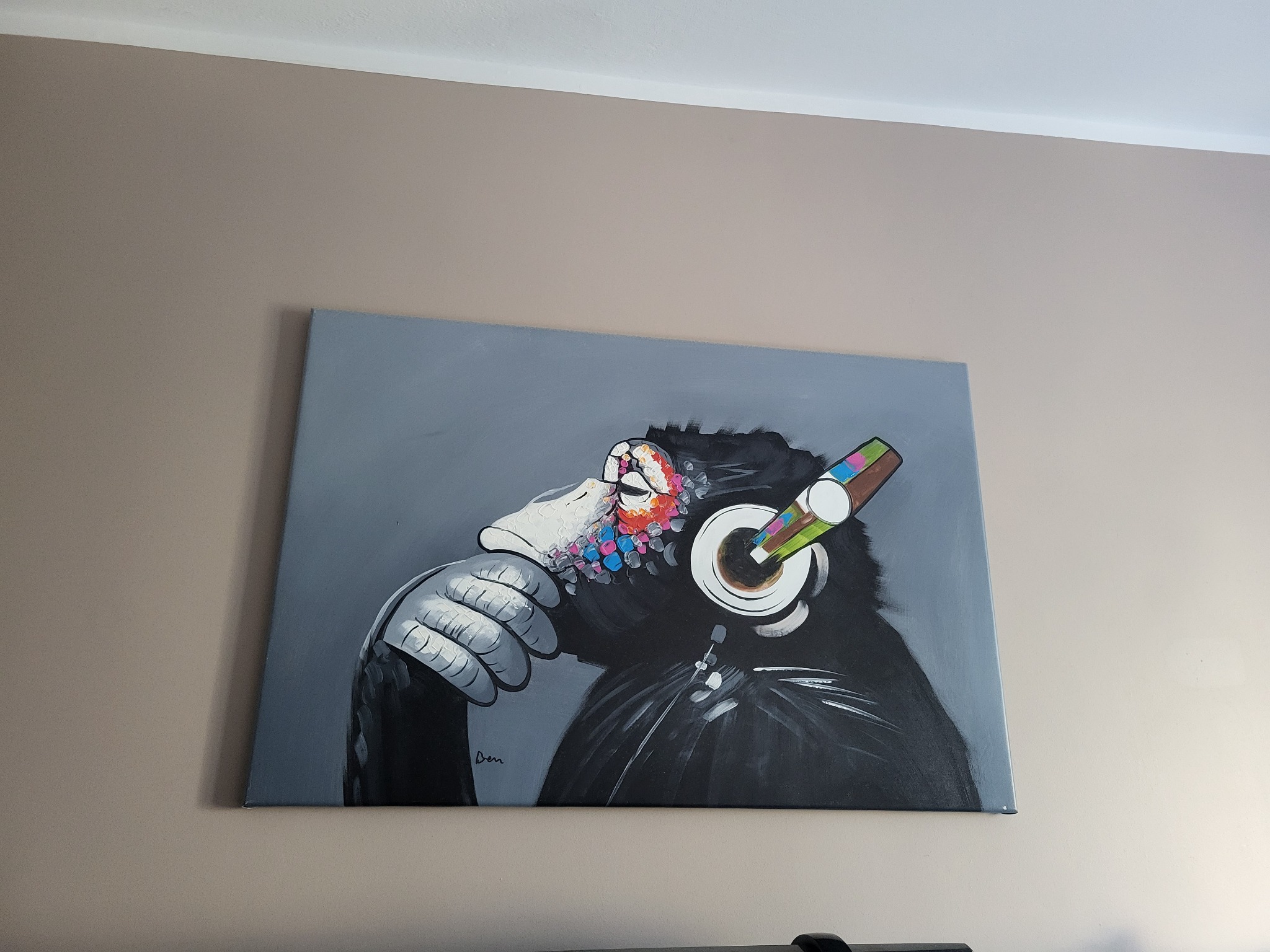 Obraz na płótnie przedstawiający małpę w słuchawkach, wiszący na beżowej ścianie, z widocznym fragmentem sufitu.