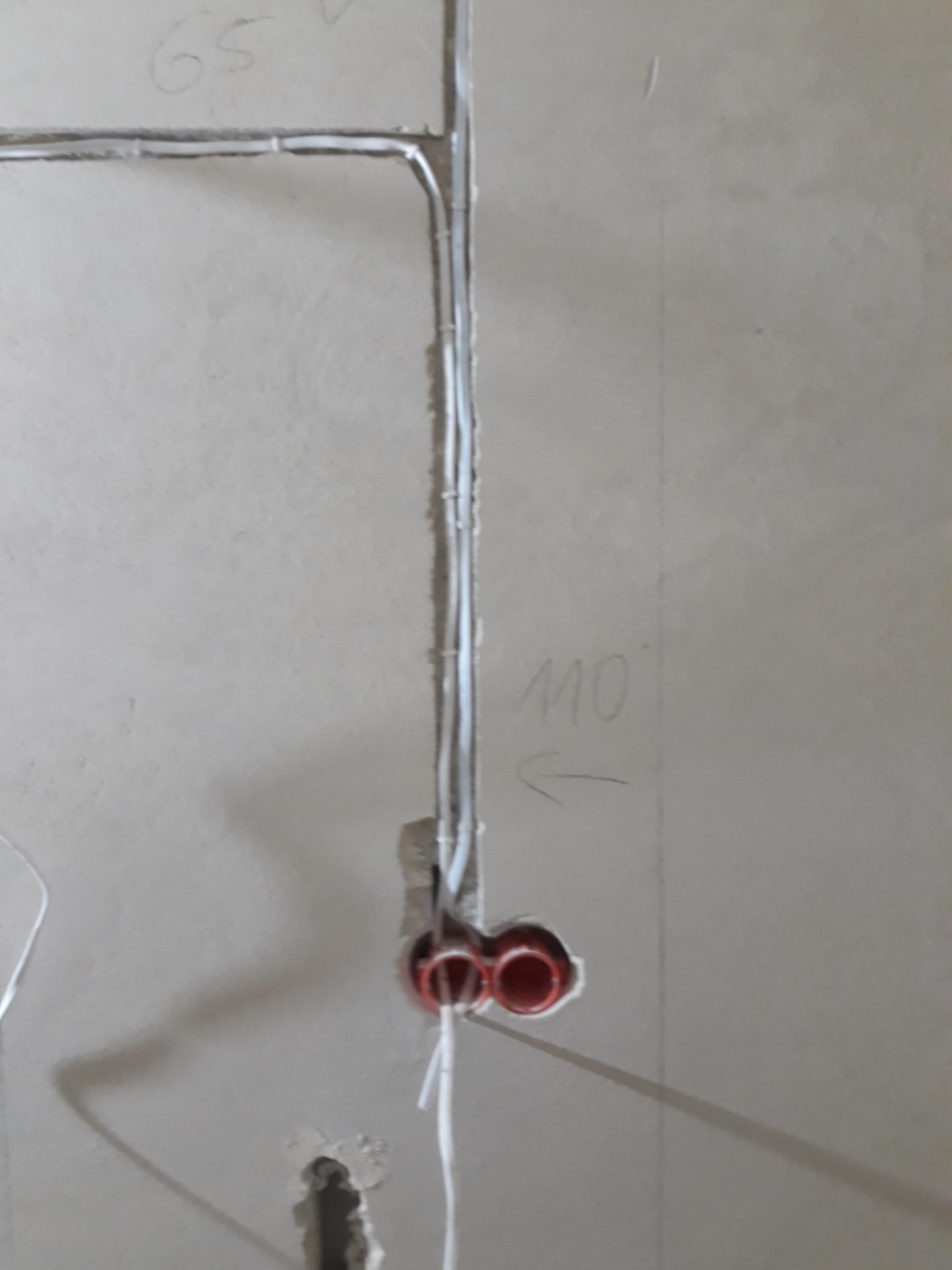 Ściana w trakcie prac instalacyjnych z widocznymi przewodami elektrycznymi w peszlach, puszkami instalacyjnymi i oznaczeniami na ścianie.