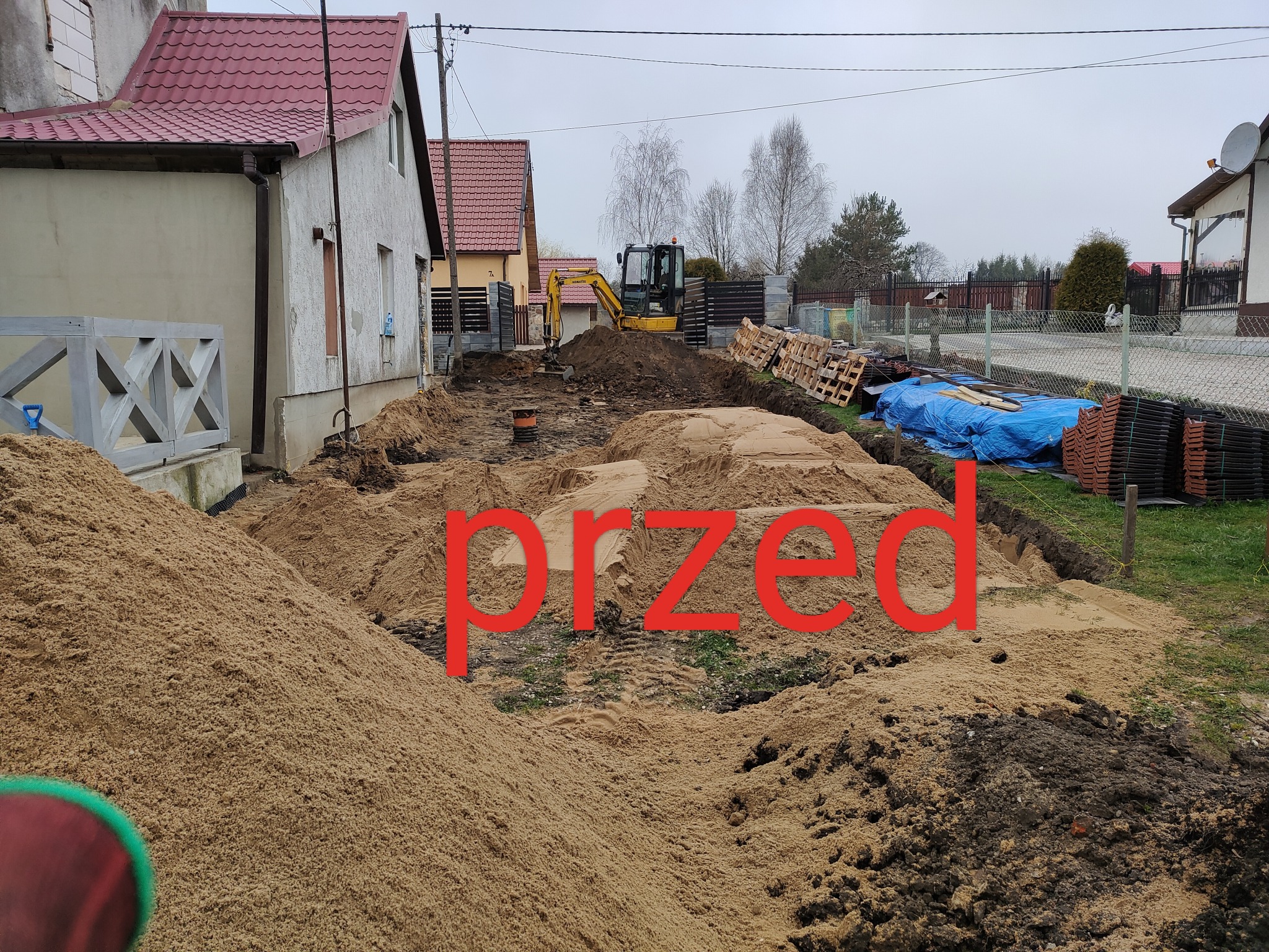 Przygotowanie terenu pod budowę domu jednorodzinnego, widoczna hałda piasku, wykop i mała koparka w tle.