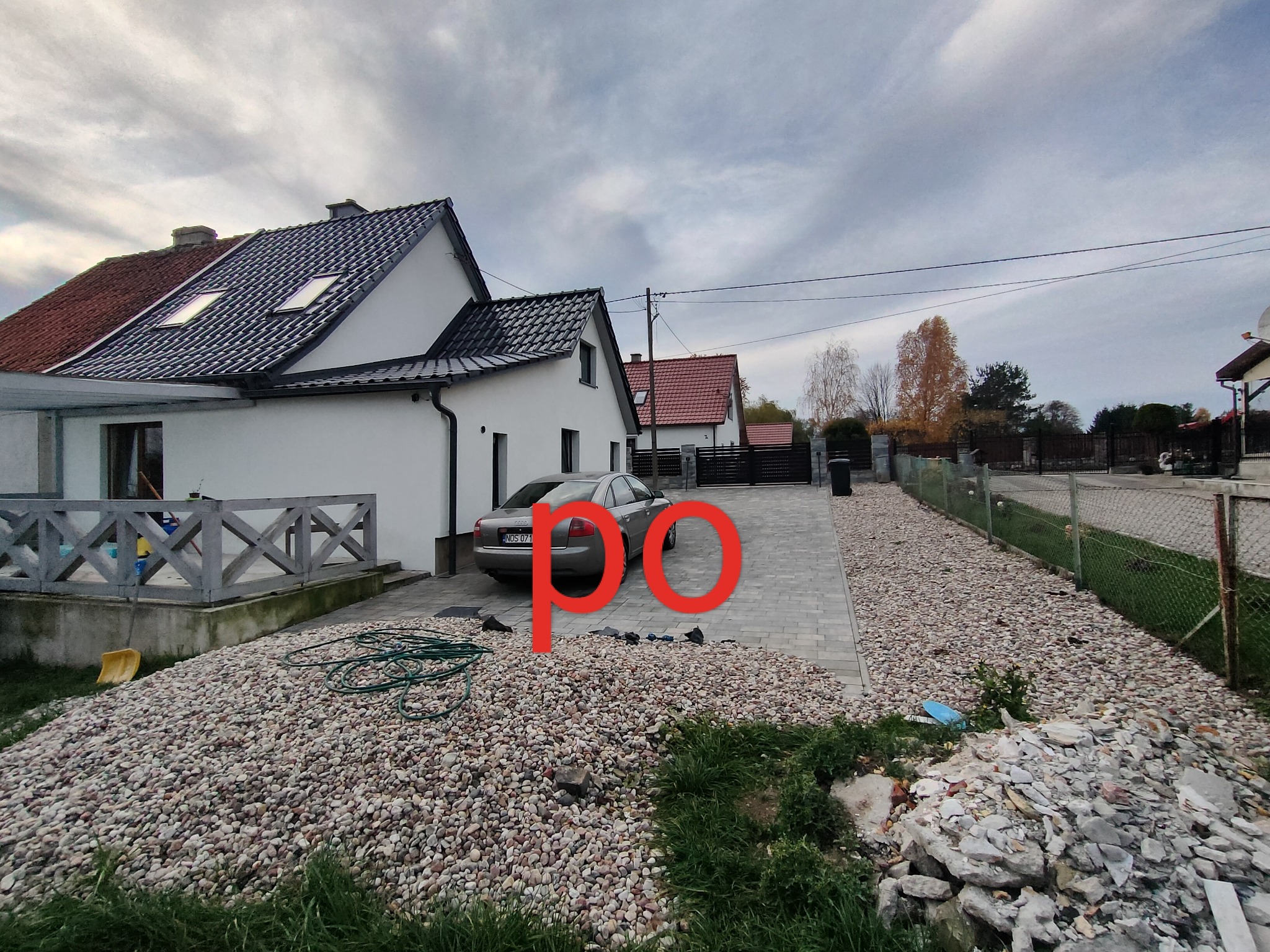 Ułożona kostka brukowa na podjeździe do domu w Miłakowie, widoczny samochód osobowy, sterta kamieni i gruzu oraz zwinięty wąż ogrodowy.