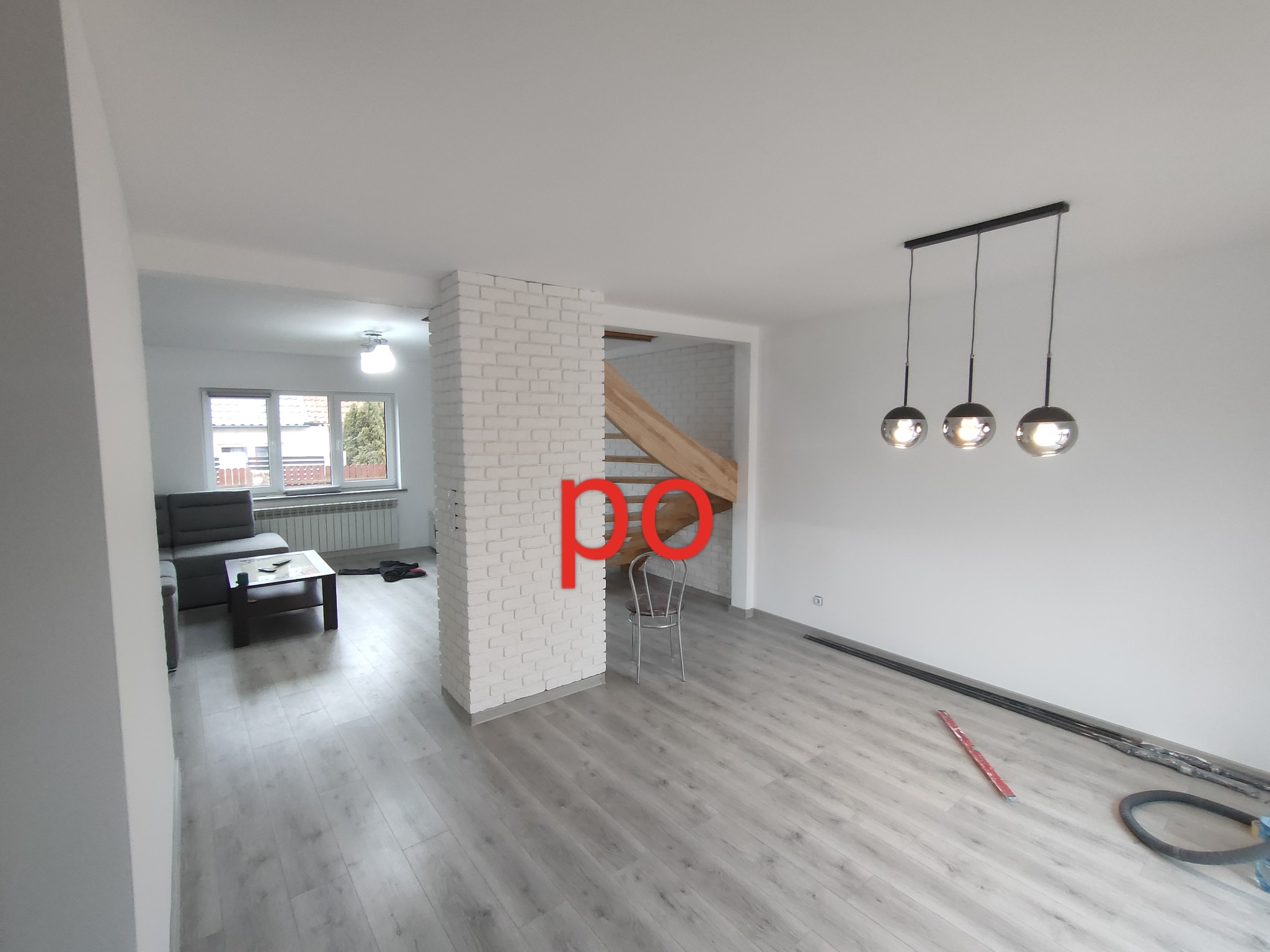 Jasne, przestronne wnętrze po remoncie z szarymi panelami podłogowymi, białą cegłą dekoracyjną i nowoczesnym oświetleniem wiszącym.