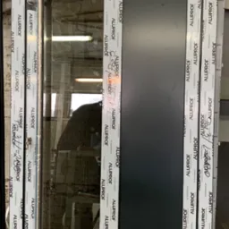 Nowe okno aluminiowe marki Aluprof, w trakcie montażu, widoczne folie ochronne i notatki na profilach.