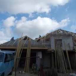 Józef Bobula - P.P.H.U BUD-MAX - Budowa domu jednorodzinnego w trakcie: widoczne drewniane elementy konstrukcji dachu, pracownicy na dachu, oraz zaparkowany niebieski bus przed budynkiem.