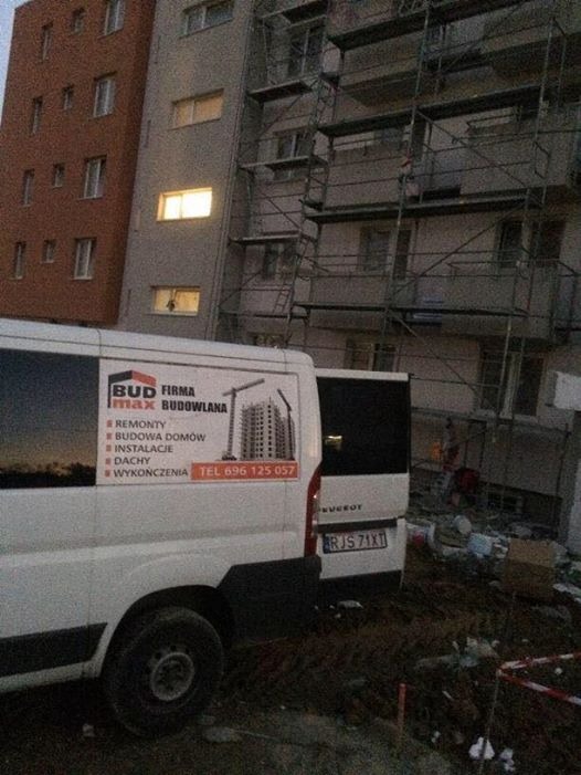 Budynek w trakcie remontu z rusztowaniami, na pierwszym planie samochód firmy remontowej 'BUD max BUDOWLANA' z numerem telefonu, widoczne gruz i teren budowy.