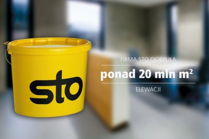 Żółte wiadro z czarnym logo STO, obok fragment ocieplenia elewacji, w tle rozmyte biuro i tekst reklamowy.