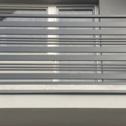 Szara, pozioma balustrada balkonowa z prostokątnych profili, widoczna na tle okna i elewacji budynku.