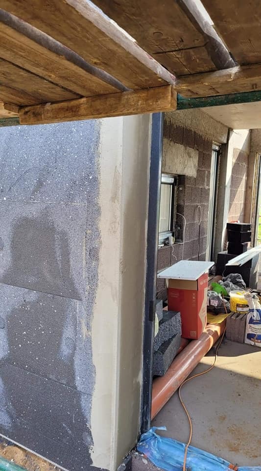 Ściana budynku w trakcie prac przygotowawczych do elewacji: bloczki z szarego styropianu, fragment rusztowania i narzędzia w tle.