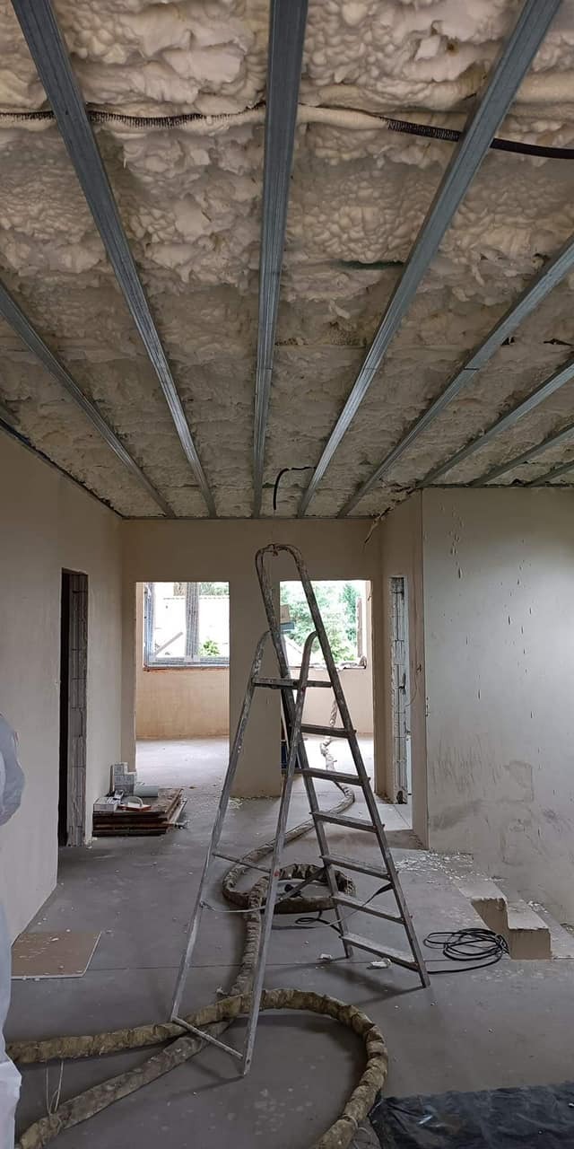 Poddasze w trakcie izolacji pianą PUR, widoczne metalowe profile sufitowe, drabina i przewód do natrysku piany.