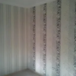 Pokój po tapetowaniu: ściany pokryte tapetą w pionowe pasy, z czego jedna ściana w szare pasy, a druga w białe pasy z szarym wzorem kwiatowym.