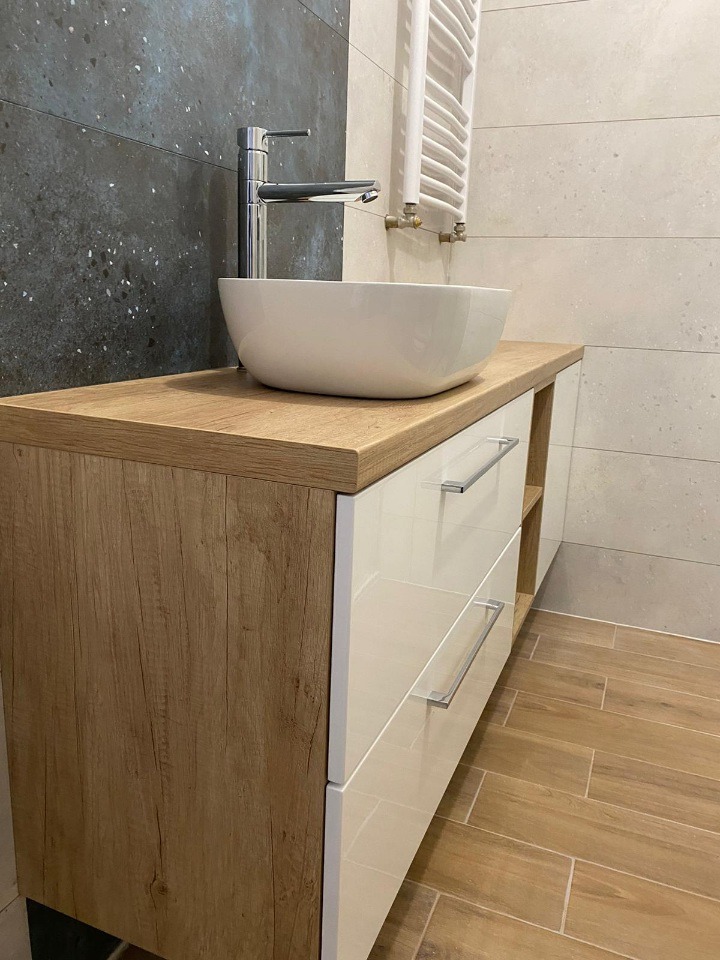 Nowoczesna szafka łazienkowa z blatem imitującym drewno, białe, lakierowane fronty szuflad i umywalka nablatowa. Minimalistyczny design, chromowana bateria.