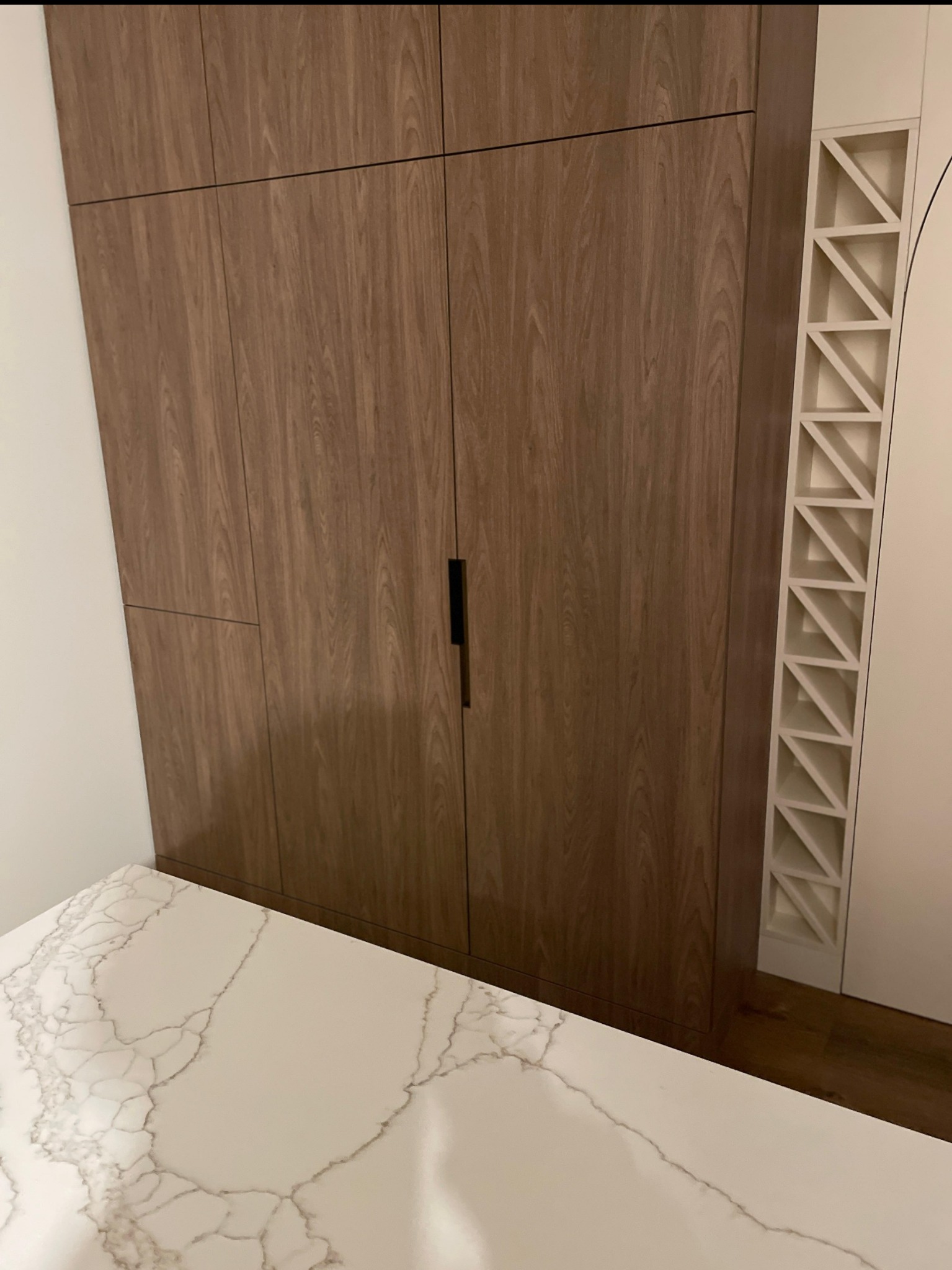 Drewniana szafa z czarnym uchwytem i biały blat z marmurowym wzorem. Obok dekoracyjny element z białymi trójkątami. Ujęcie z bliska, wnętrze.