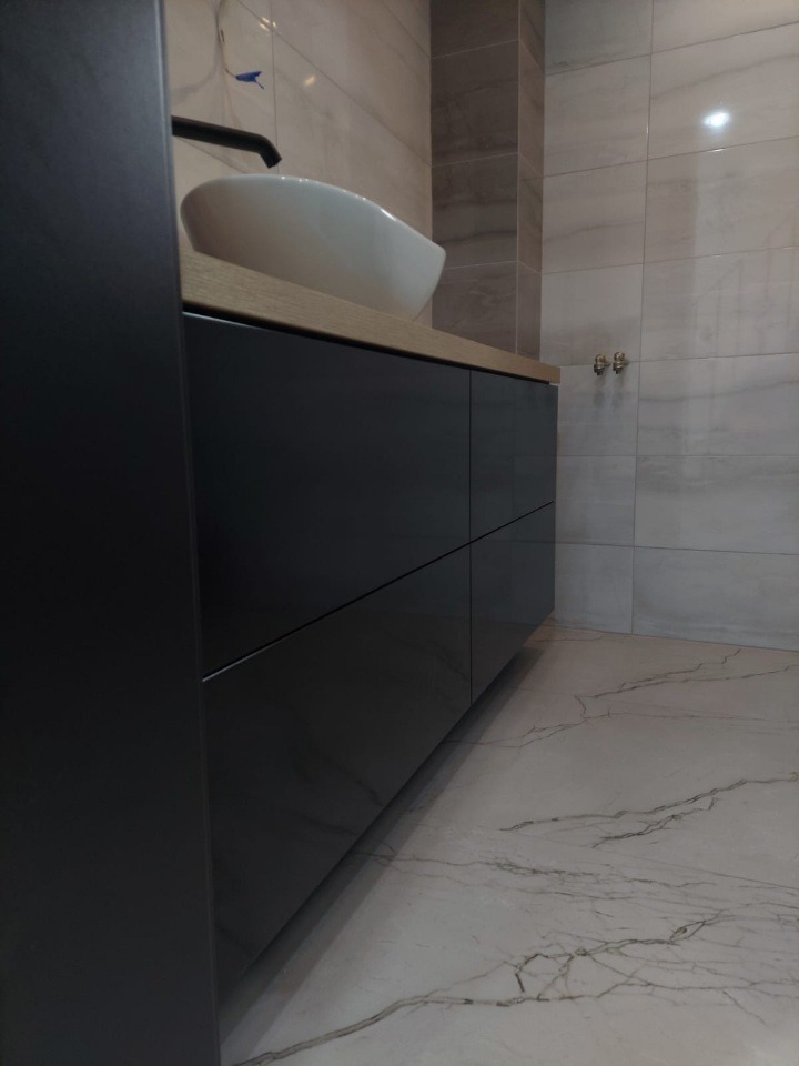 Nowoczesna łazienka: czarna szafka pod umywalkę z blatem z jasnego drewna, biała umywalka nablatowa, marmurowe płytki na podłodze i ścianie. Minimalistyczny design.