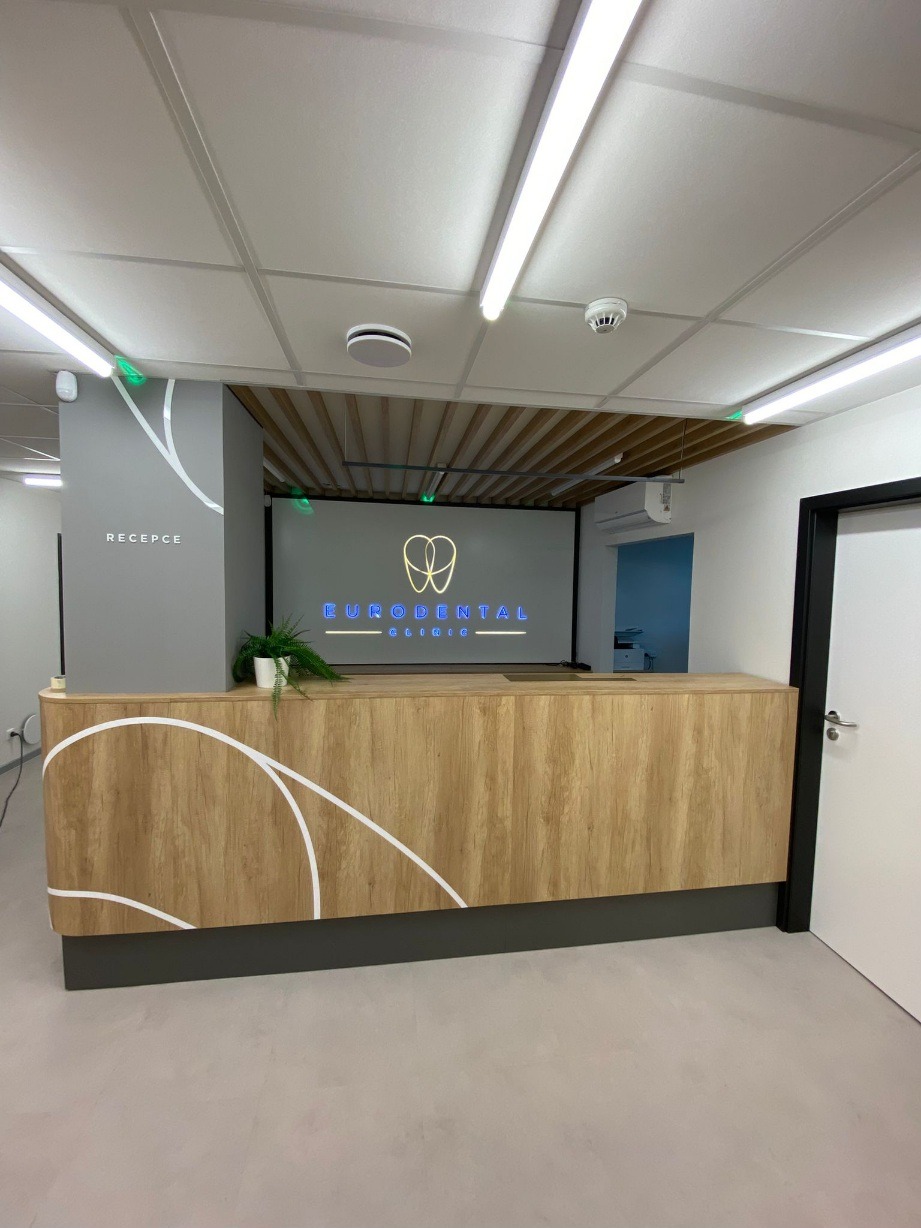 Drewniana lada recepcyjna z białymi zdobieniami w Krępicach. Nowoczesny design, oświetlenie LED i minimalistyczny styl. Widok na logo kliniki dentystycznej.