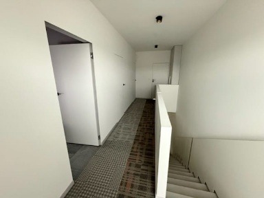 Biały korytarz z ukrytymi drzwiami i wzorzystym dywanem, widok z góry schodów. Minimalistyczny design, nowoczesne oświetlenie punktowe.