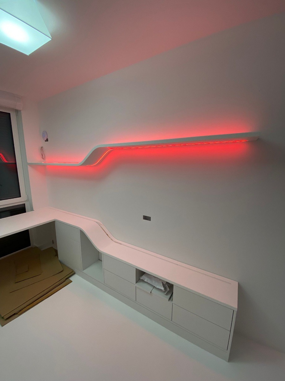 Białe meble na wymiar z podświetleniem LED w kolorze czerwonym, tworzące nowoczesny design. Widoczne szafki, półki i blat roboczy. Minimalistyczne wnętrze.