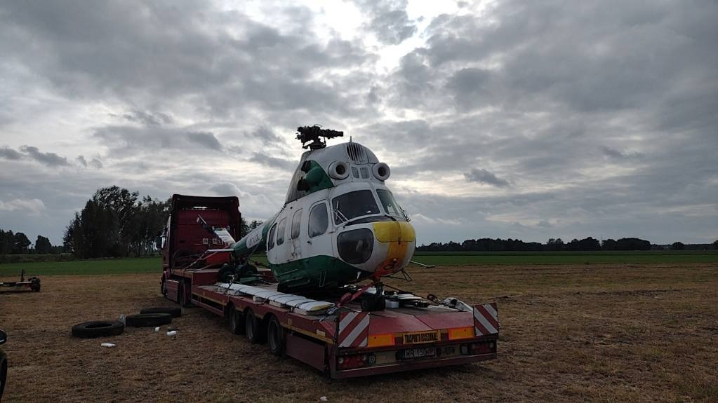 Transport uszkodzonego helikoptera Mi-2 na niskopodwoziowej naczepie w pochmurny dzień.