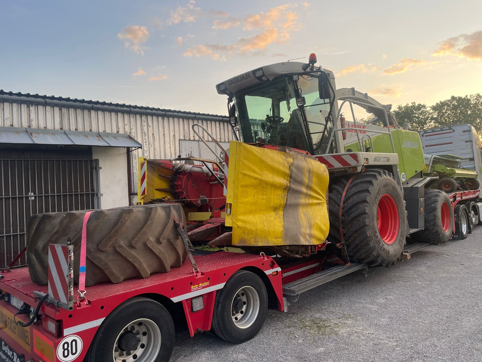 Kombajn rolniczy marki Jaguar przewożony na niskopodwoziowej platformie transportowej z dodatkowymi oponami zabezpieczonymi różowymi pasami.