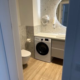 Elite painting - Nowoczesna łazienka w odcieniach szarości i beżu z okrągłym podświetlanym lustrem, pralką pod blatem i wiszącą toaletą.