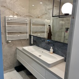 Elite painting - Nowoczesna łazienka w Gdańsku z marmurowymi płytkami, białym blatem umywalkowym i grzejnikiem drabinkowym. W lustrze odbija się kabina prysznicowa.