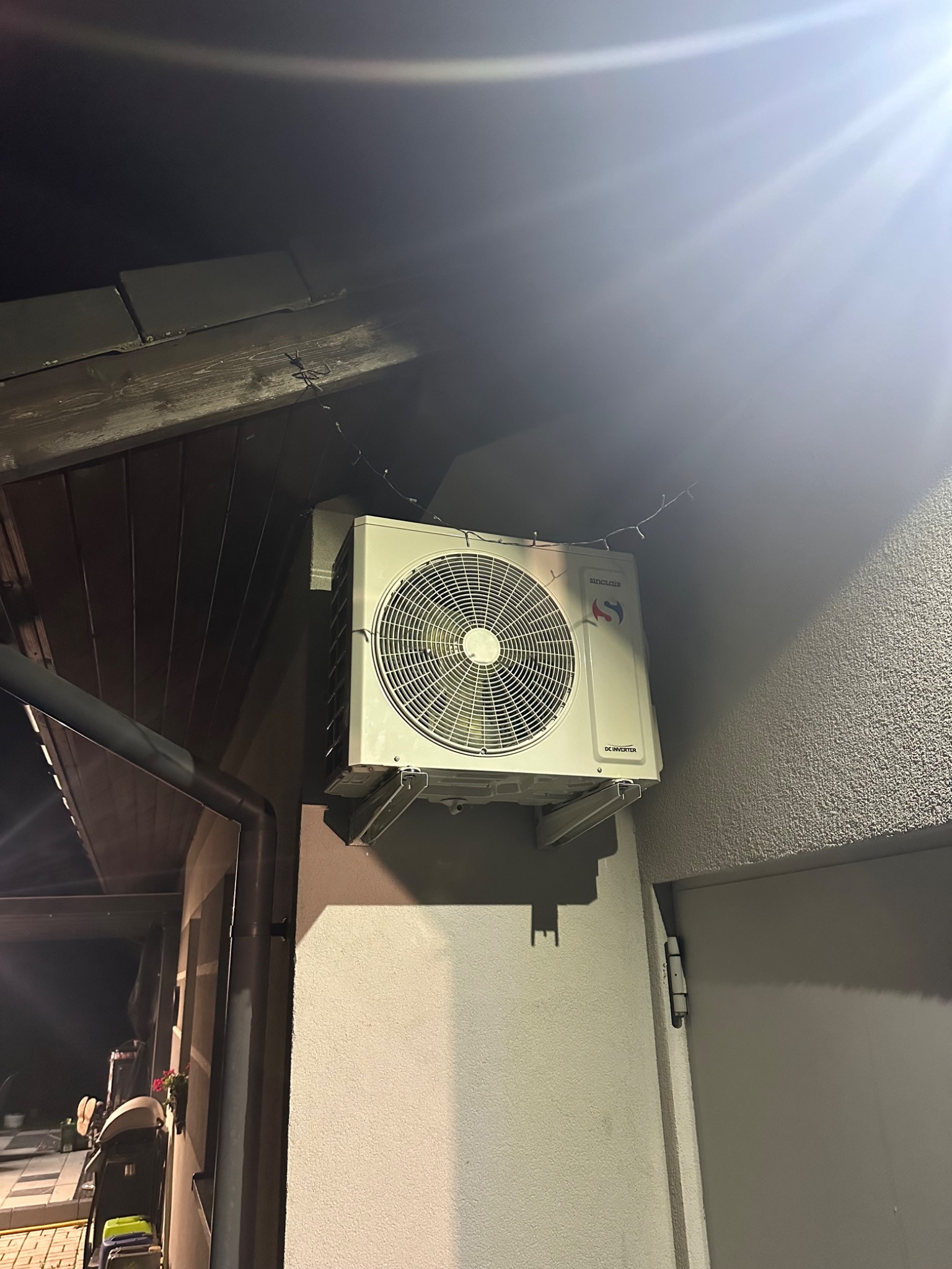 Zewnętrzna jednostka klimatyzacji Sinclair zamontowana na ścianie budynku z widocznymi elementami elewacji i dachu.