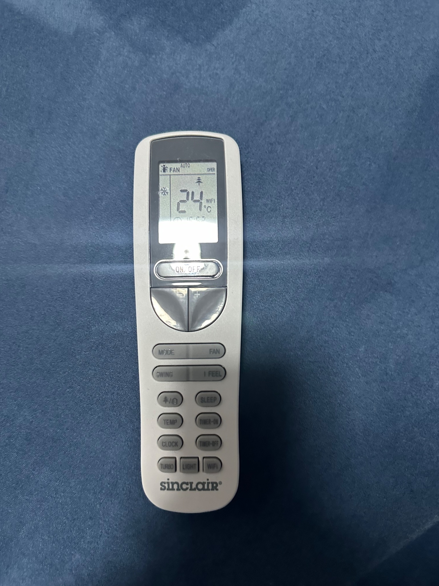 Pilot do klimatyzacji Sinclair z wyświetlaczem ustawionym na 24 stopnie Celsjusza, leżący na niebieskim materiale.