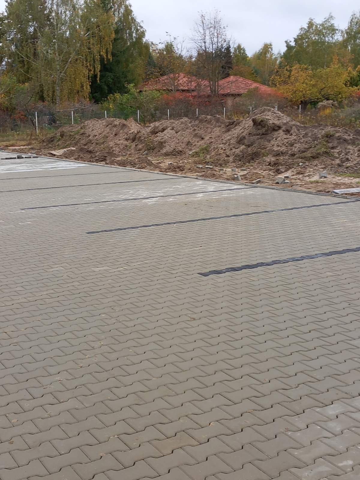 Nowo ułożona szara kostka brukowa w jodełkę z czarnymi dylatacjami na parkingu, widoczna sterta ziemi w tle.