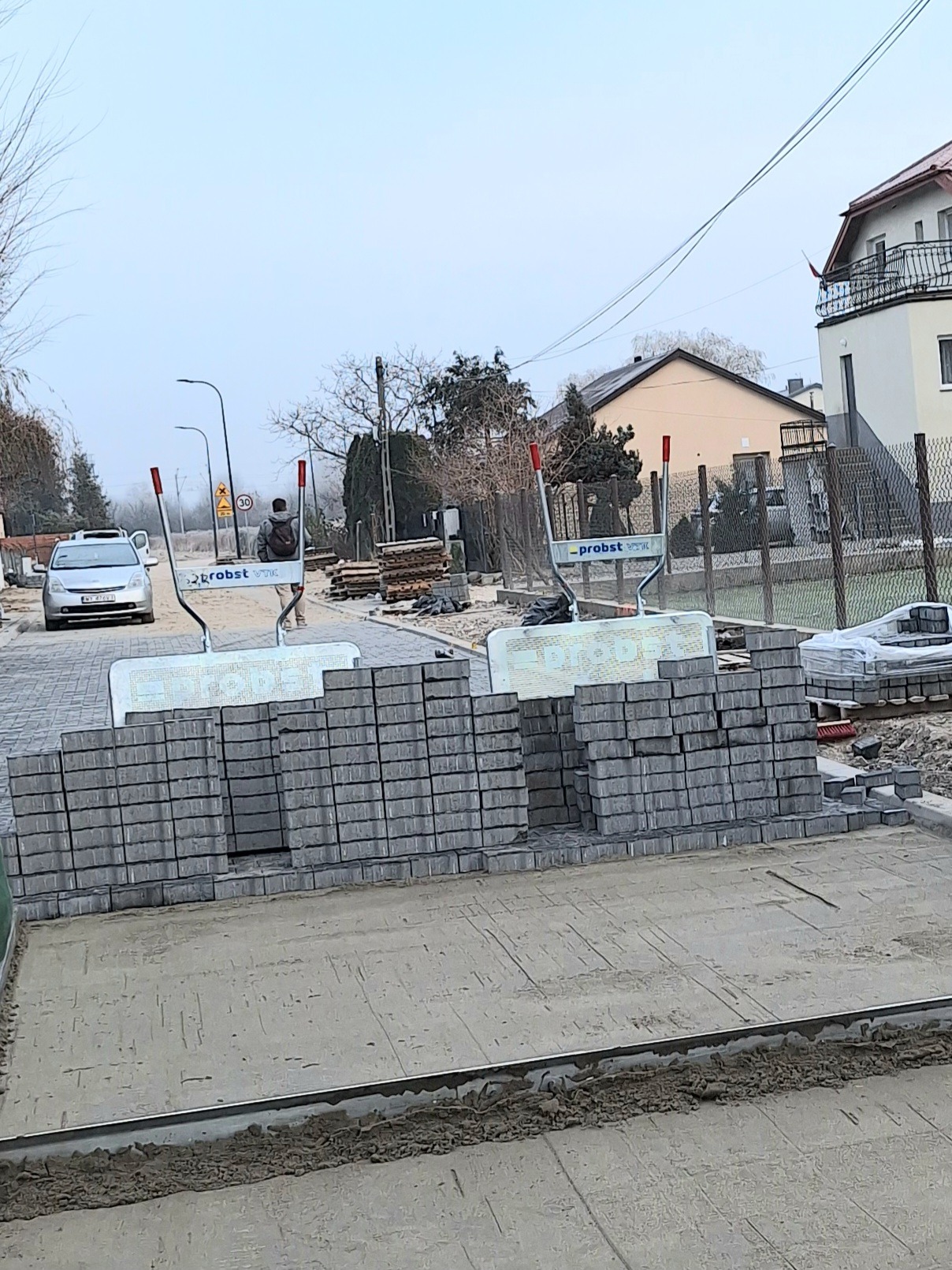 Przygotowany teren pod układanie kostki brukowej z ułożonymi paletami kostki i widocznym mężczyzną w oddali.