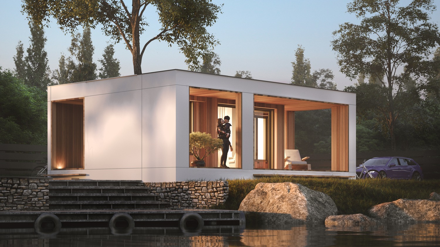 Nowoczesny dom modułowy z płaskim dachem, widok od strony jeziora, na tarasie stoi para, obok zaparkowany samochód.