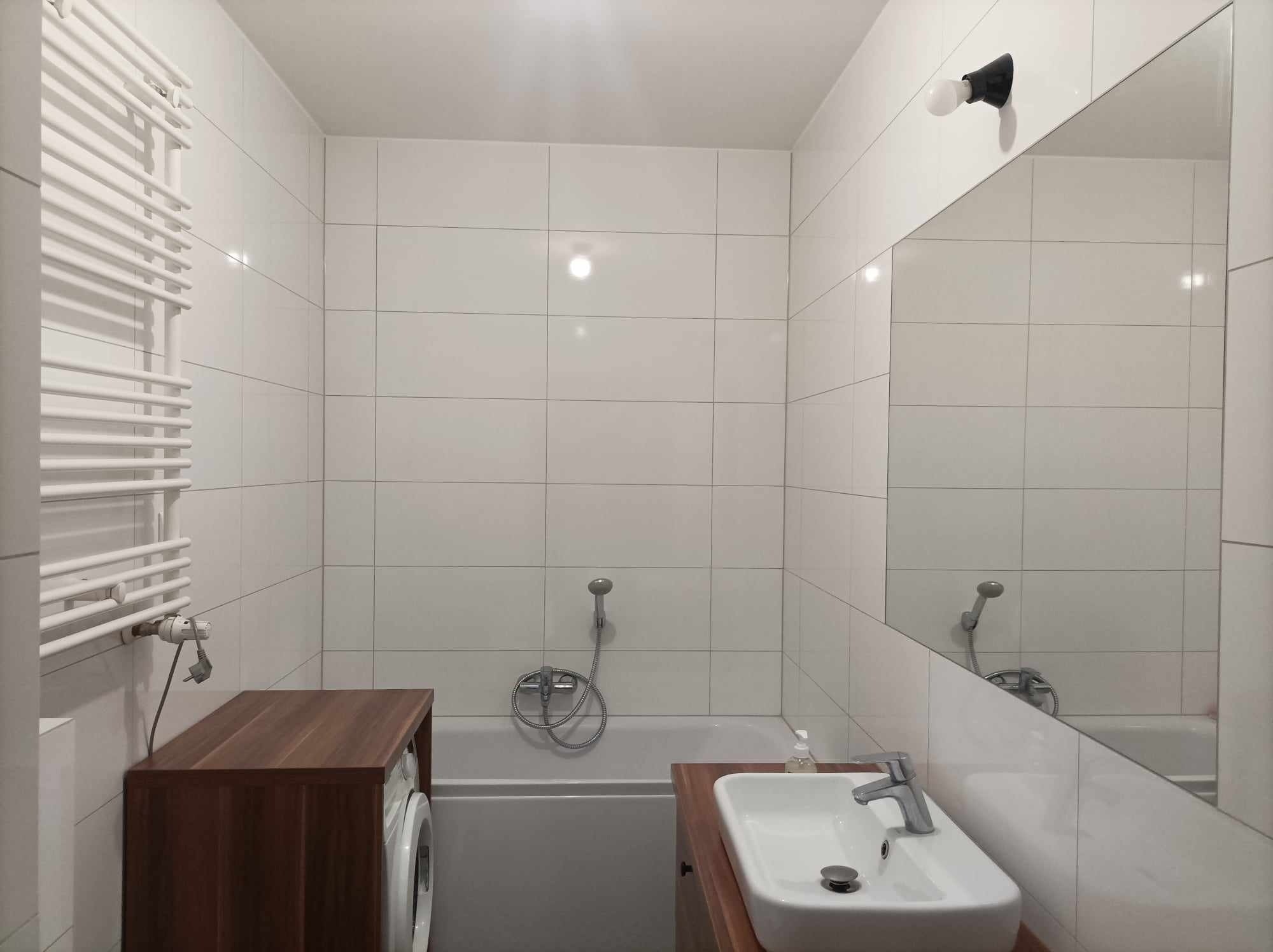 Nowoczesna łazienka z białą armaturą, brązowymi szafkami i grzejnikiem drabinkowym, pralka ukryta w zabudowie.