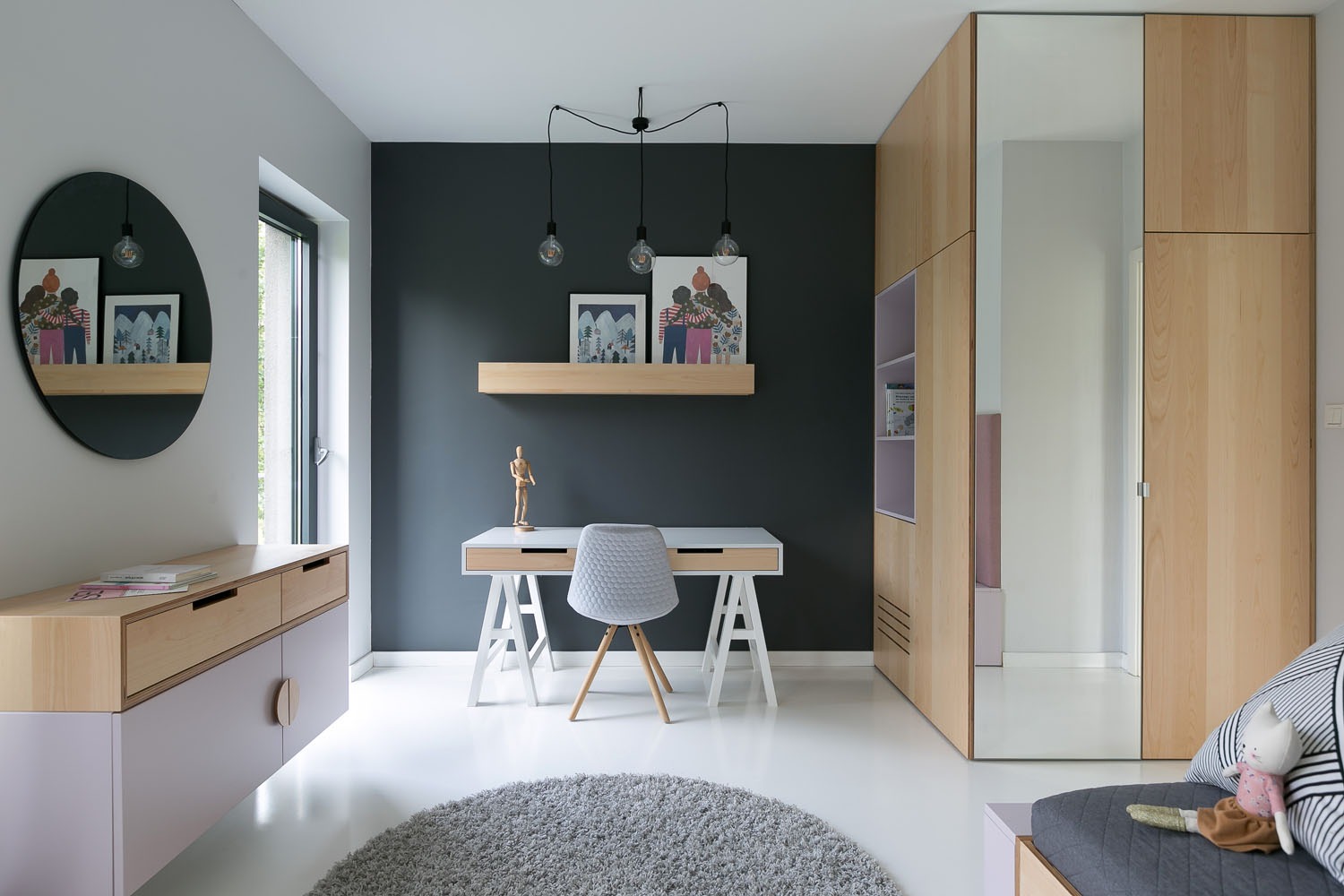 Nowoczesny pokój z biurkiem na kozłach, szarą ścianą i drewnianymi meblami z pastelowymi akcentami, okrągłe lustro z półką i designerskie lampy wiszące.