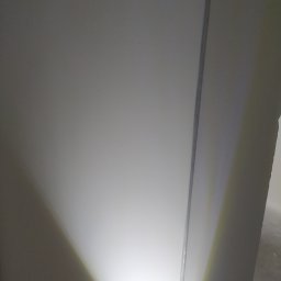 RW remonty i wykończenia wnętrz - Ściana po obróbce, oświetlona punktowo od dołu, widoczna krawędź ściany. Powierzchnia gładka, gotowa do malowania. Minimalistyczne ujęcie.