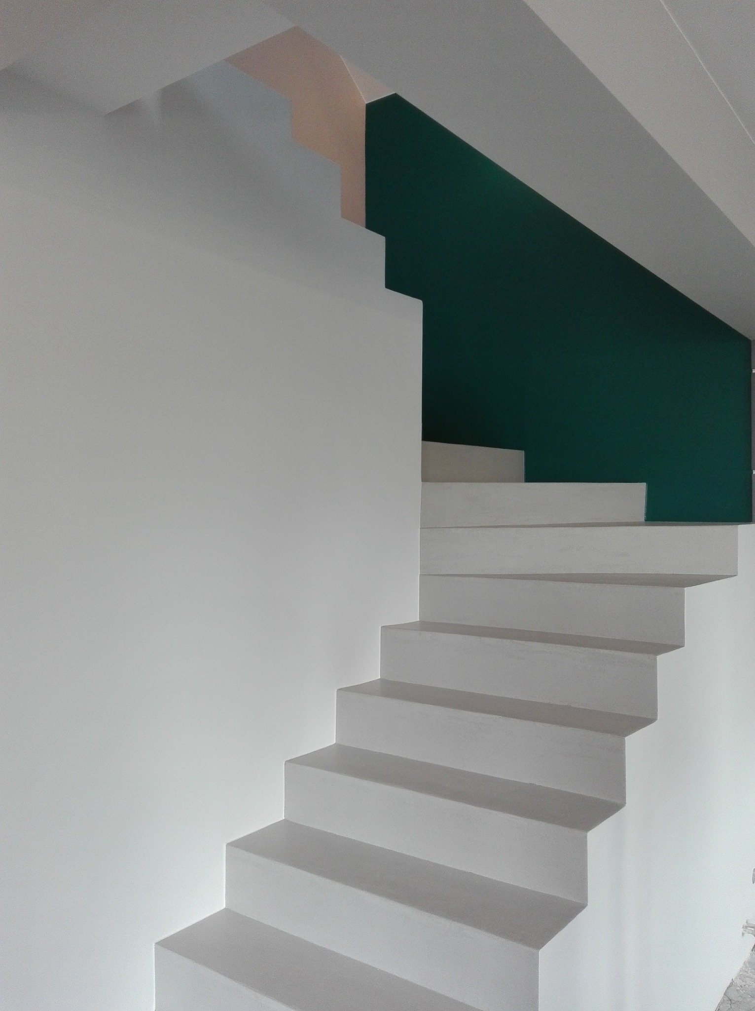 Minimalistyczne schody z gładkimi, białymi ścianami, akcentowane zieloną ścianą w tle i subtelnym odcieniem różu na górze, tworzą nowoczesne wnętrze.