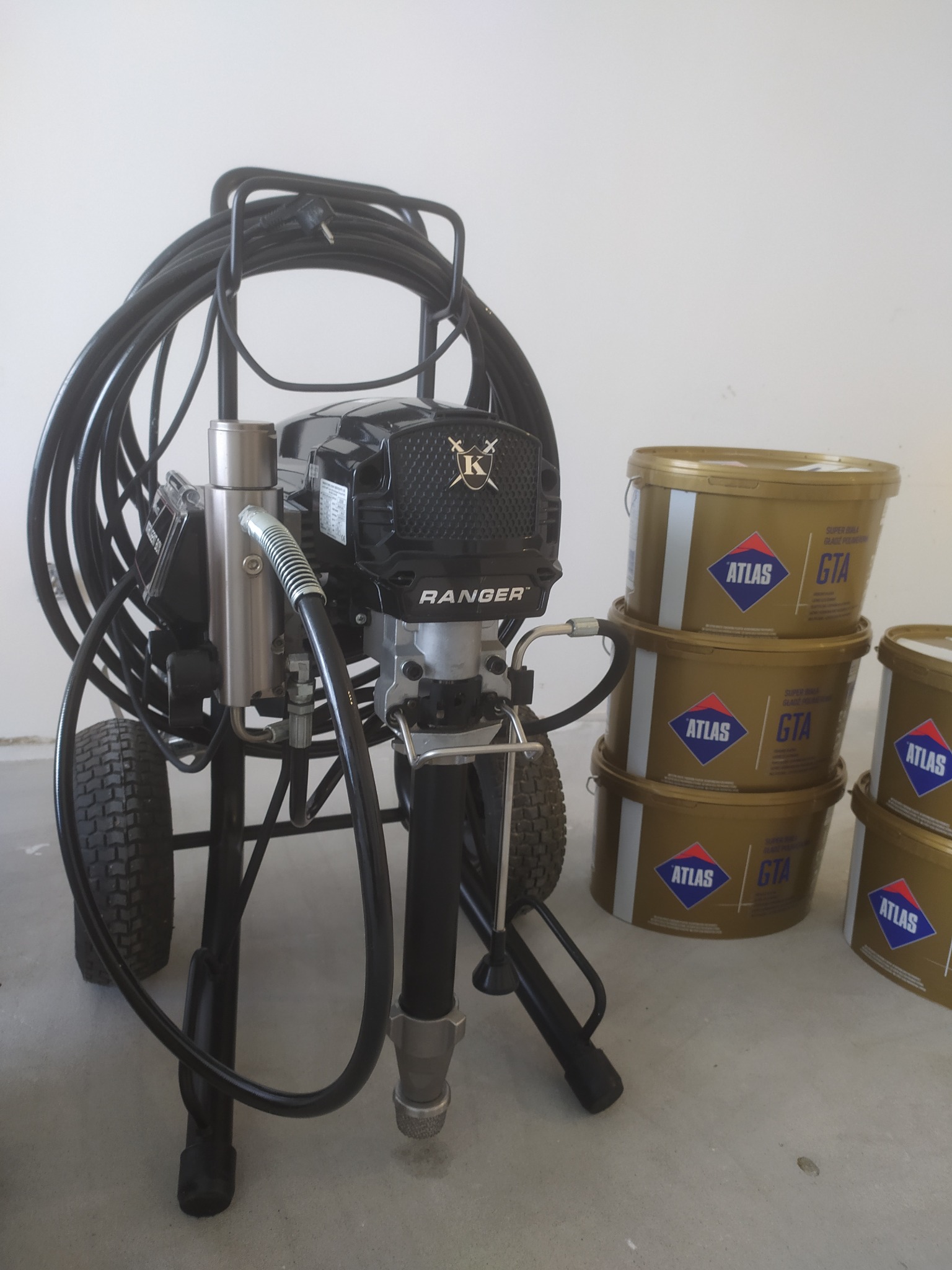 Agregat malarski Ranger na tle wiader z masą Atlas GTA. Sprzęt do natryskowego nakładania materiałów wykończeniowych, gotowy do użycia na budowie lub w mieszkaniu.