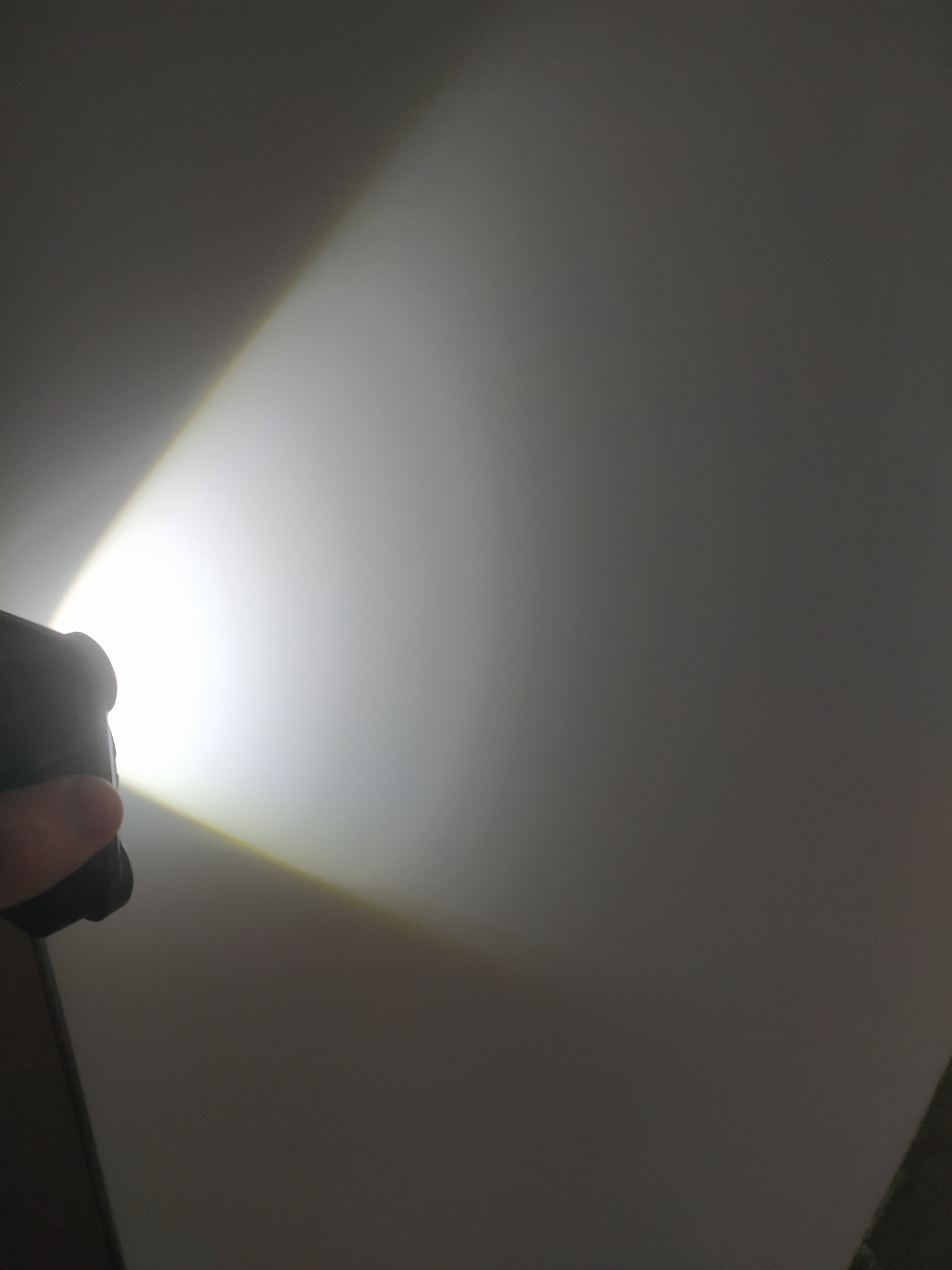 Lampa inspekcyjna oświetla gładką, szarą powierzchnię ściany pod kątem, ukazując jej strukturę i ewentualne niedoskonałości. Kontrast światła i cienia.