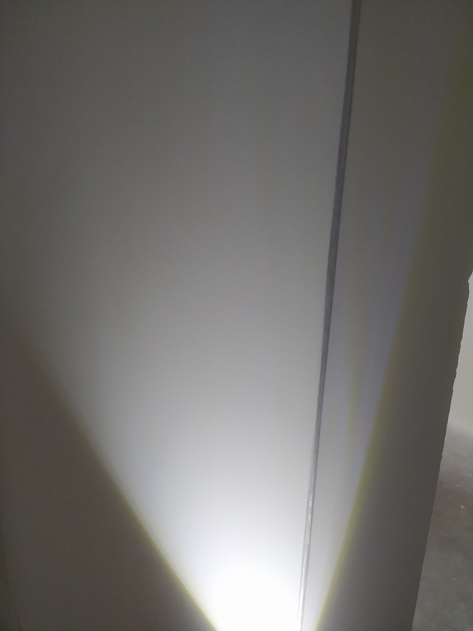 Ściana po obróbce, oświetlona punktowo od dołu, widoczna krawędź ściany. Powierzchnia gładka, gotowa do malowania. Minimalistyczne ujęcie.