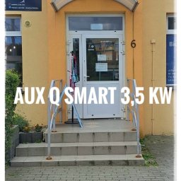 KLIMA STAR - Zewnętrzna jednostka klimatyzacji AUX Q SMART 3.5 KW zamontowana nad wejściem do budynku z żółtą elewacją, widoczny szyld firmy.
