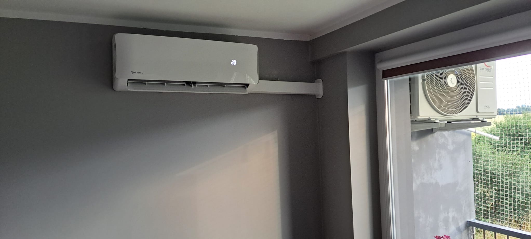 Zamontowany klimatyzator ROTENSO na ścianie w mieszkaniu w Elblągu, widoczny również klimatyzator na balkonie za oknem.