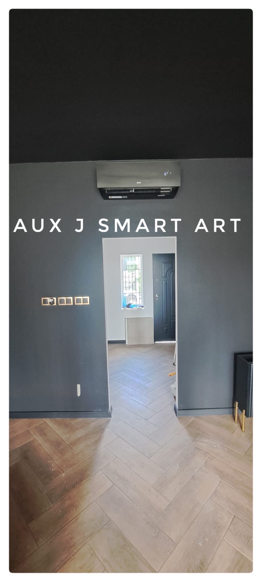 Zamontowany klimatyzator AUX J SMART ART na ciemnej ścianie w pokoju z parkietem ułożonym w jodełkę.