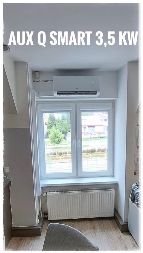 Zamontowany biały klimatyzator AUX Q SMART 3,5 KW nad oknem w pokoju z grzejnikiem pod parapetem.