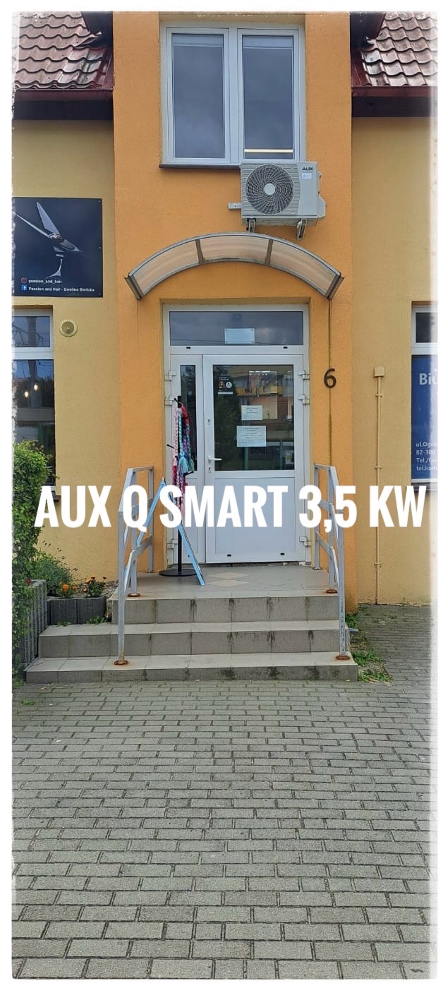 Zewnętrzna jednostka klimatyzacji AUX Q SMART 3.5 KW zamontowana nad wejściem do budynku z żółtą elewacją, widoczny szyld firmy.