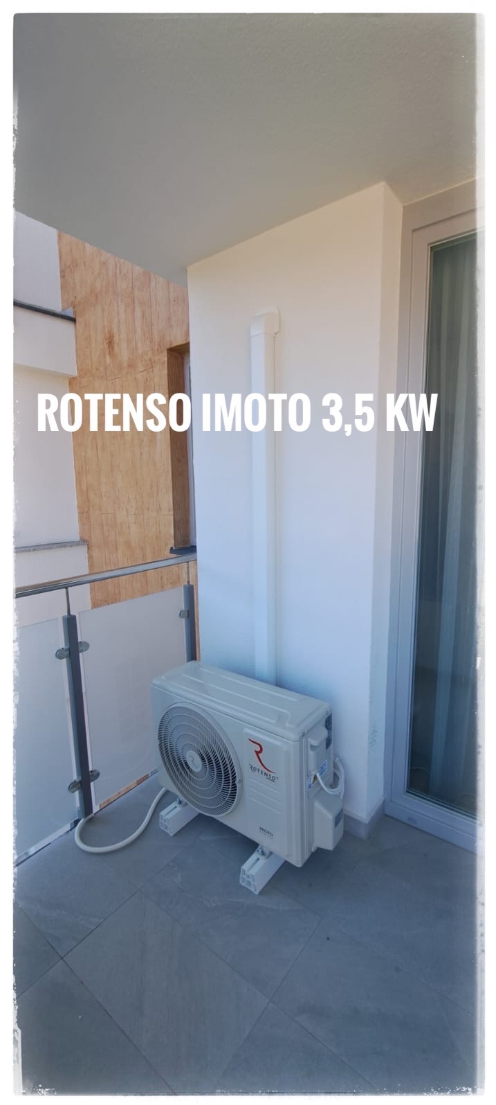 Zewnętrzna jednostka klimatyzacji Rotenso Imoto 3.5 kW, zamontowana na balkonie z szarą podłogą, widoczna biała rura odprowadzająca skropliny.