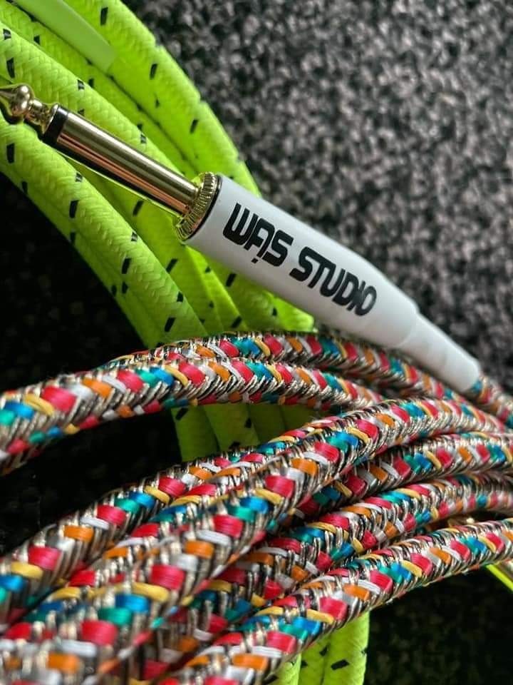 Kabel instrumentalny z wtyczką jack, opleciony kolorowym, wzorzystym materiałem, obok neonowo-zielonego kabla, z logo 'WAS STUDIO' na białej obudowie wtyczki.