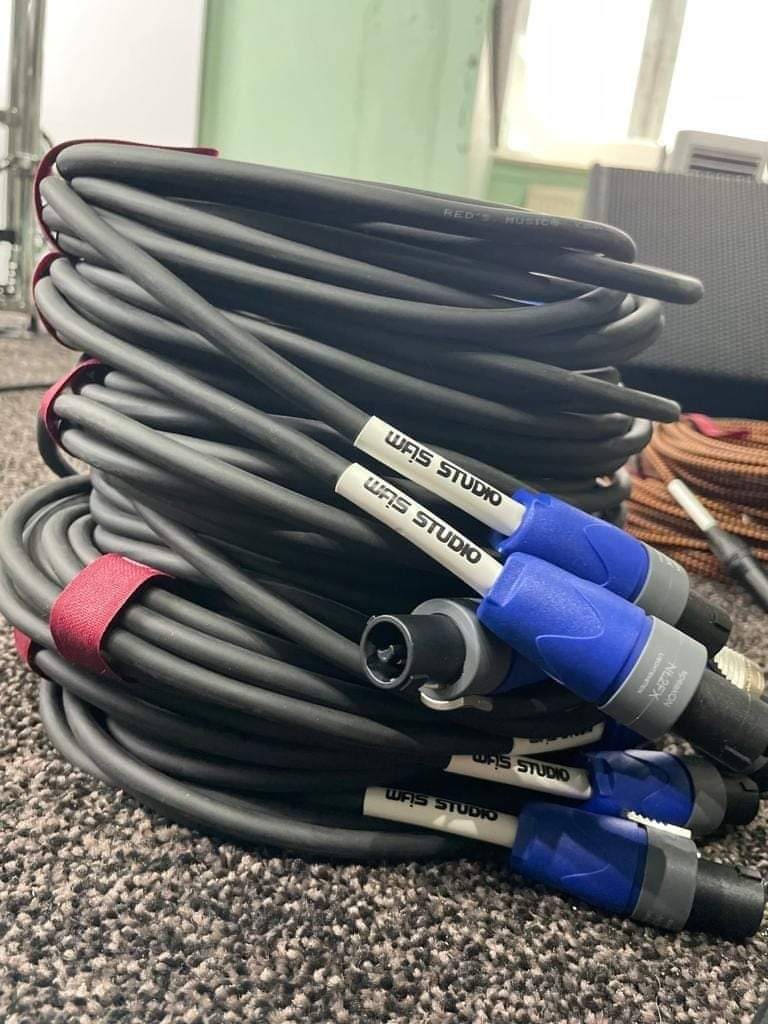 Zwinięte kable audio z wtyczkami Neutrik Speakon NL2FX, oznaczone jako 'WAS STUDIO', leżące na dywanie.