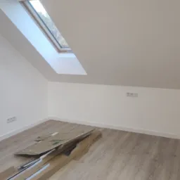 Pokój na poddaszu z oknem dachowym i panelami podłogowymi. Widoczne kartony po roletach okiennych i worki na śmieci. Świeżo pomalowane ściany na biało.
