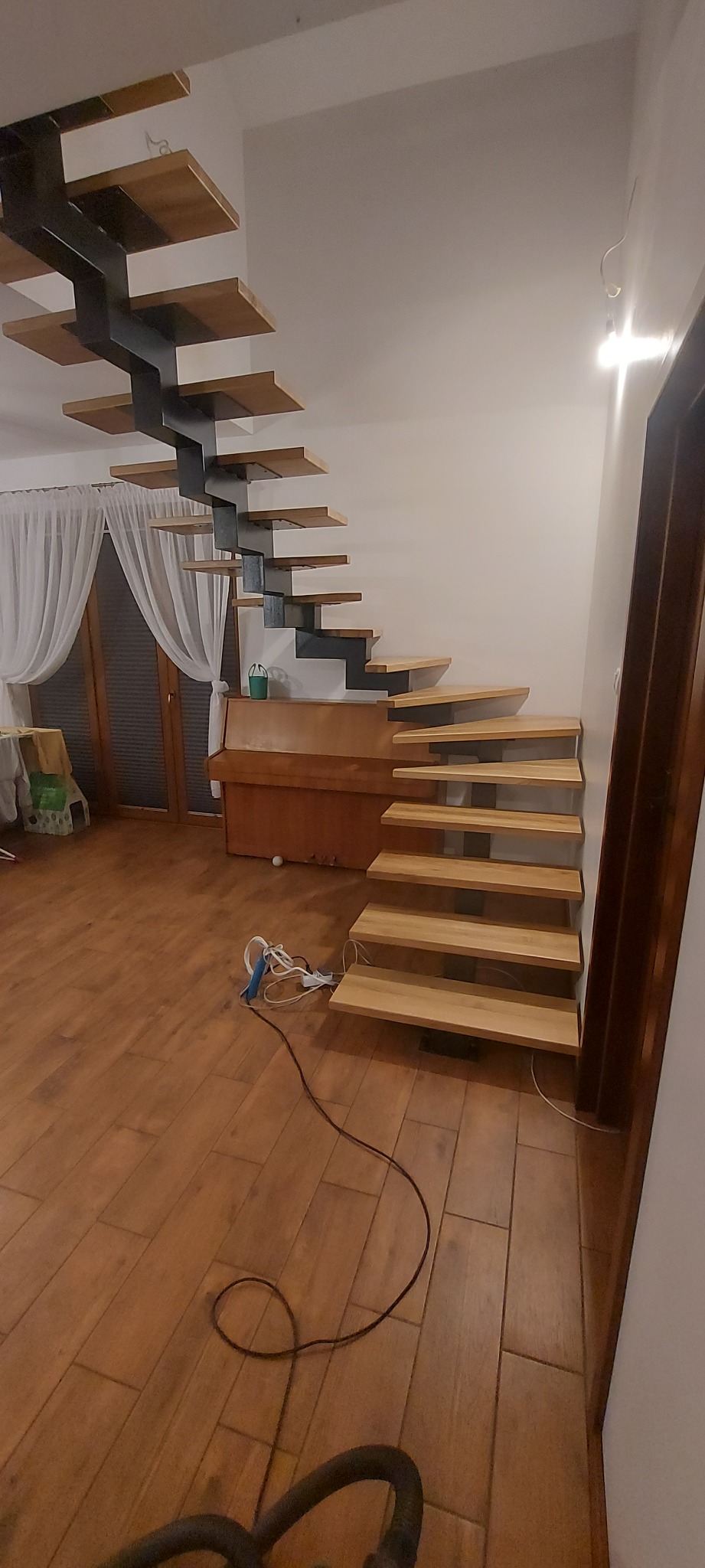 Nowoczesne schody z drewnianymi stopniami i metalową konstrukcją w jasnym wnętrzu, widoczne przewody narzędzi na podłodze.