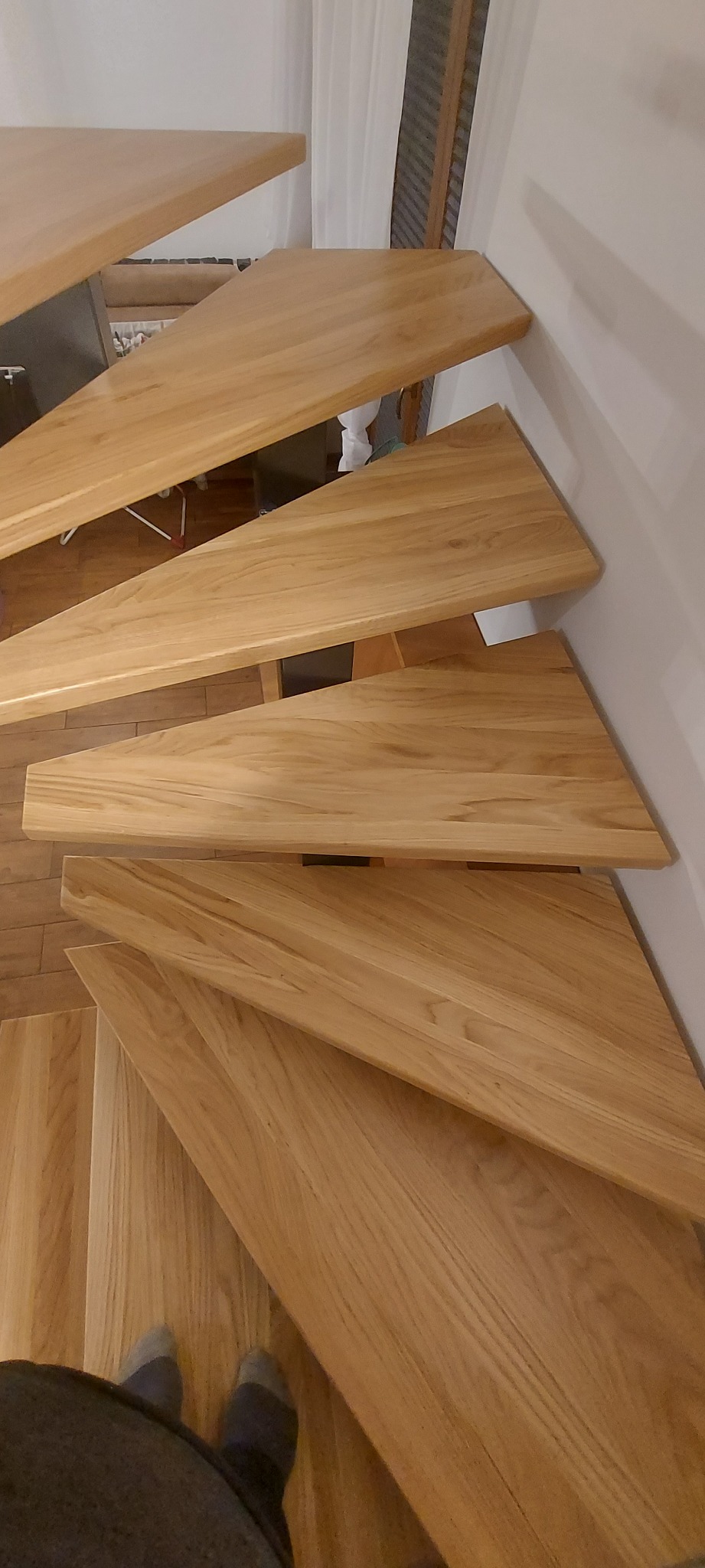 Widok z góry na drewniane schody wachlarzowe z jasnego drewna dębowego, z widocznymi detalami słojów drewna i fragmentem osoby w dolnej części kadru.