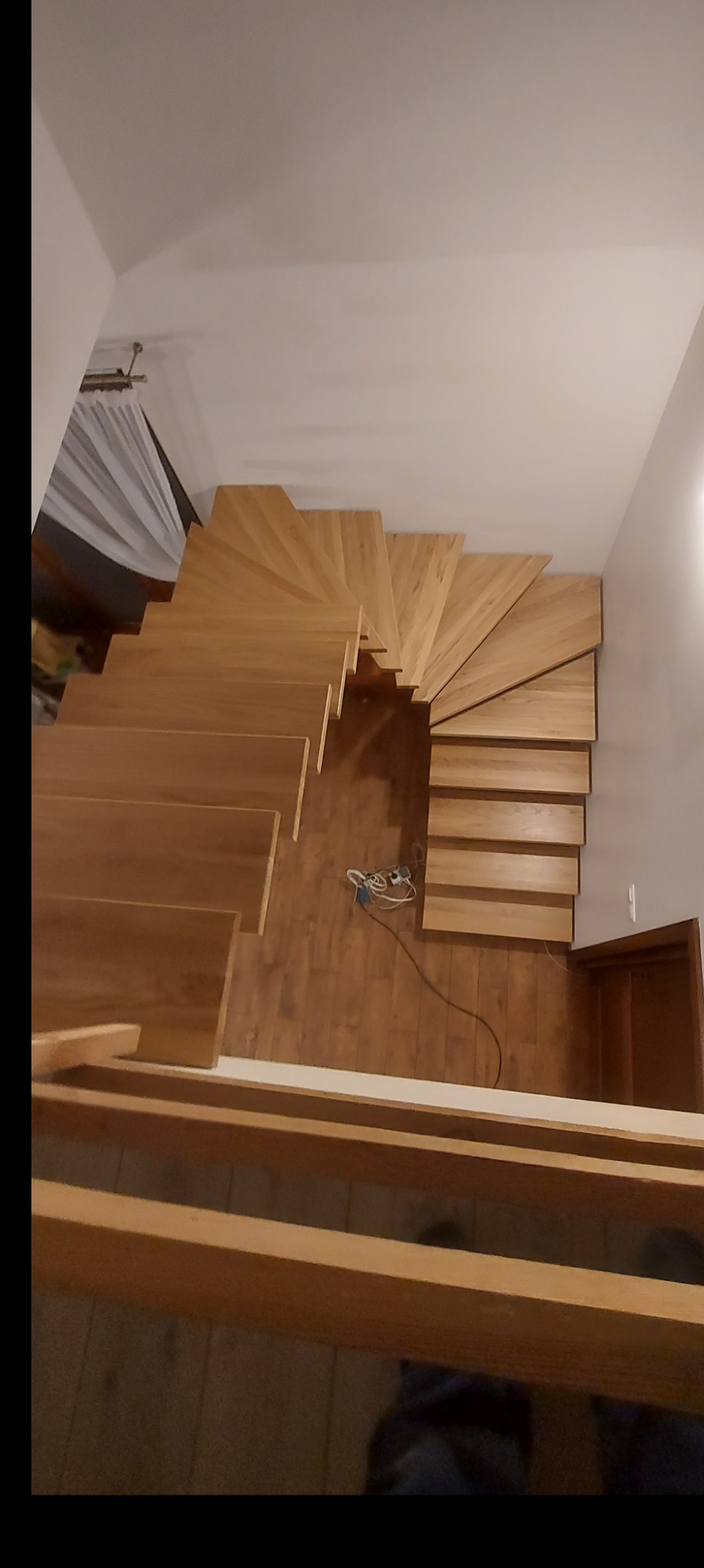 Widok z góry na jasne, drewniane schody z zakrętem, prowadzące na wyższą kondygnację domu. Na podłodze widoczne kable i narzędzia, sugerujące trwający montaż.